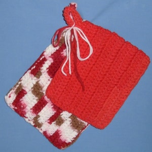 May include: Two handmade crochet potholders. One is solid red, the other is a mix of red, white, and brown. Both have a loop for hanging and are tied together with white yarn. The potholders are likely used for handling hot cookware.