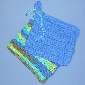 May include: Two handmade crochet potholders. One is solid light blue with a loop and tie. The other is striped with shades of blue, green, and brown. The potholders are square and appear to be made of cotton yarn.