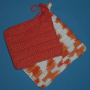 May include: Two handmade crochet pot holders. One is a solid coral color with a loop for hanging. The other is white with an orange and coral pattern. The pot holders are square and appear to be made of cotton yarn.