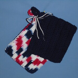 May include: Crocheted potholder set. One potholder is solid navy blue, the other features a red, white, and navy blue pattern. The potholders are tied together with white string. A yellow pin is attached to the navy blue potholder.