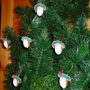 May include: A Christmas tree decorated with handmade ornaments shaped like Santa Claus. The ornaments are made from nutshells and have a white face with a red hat and white beard. The tree is decorated with green pine needles and has a brown wooden background.