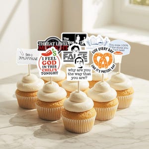 May include: Cupcakes with white frosting and decorative toppers featuring phrases like "I FEEL GOD IN THIS CHILI'S TONIGHT" and "LIVE EVERY DAY LIKE IT'S PRETZEL DAY." The cupcakes are arranged on a marble surface.