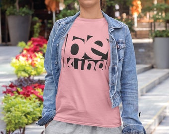 Könnte beinhalten: Ein rosa T-Shirt mit dem Aufdruck "be kind" in schwarzen Buchstaben. Die Buchstaben überlappen sich und sind in einem einzigartigen Design angeordnet.