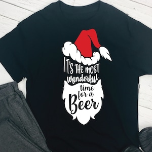 May include: Black t-shirt with a white graphic of a Santa Claus beard and hat. The text reads "It's the most wonderful time for a Beer."