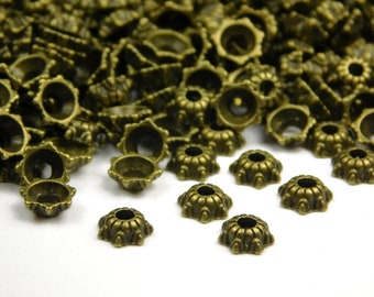 May include: A large pile of antique gold-toned metal bead caps with a few bead caps in the foreground. The bead caps have a starburst design.