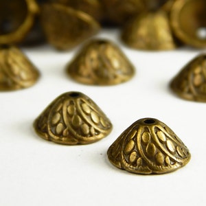 May include: A group of small, gold-colored metal cones with an intricate, embossed design. The cones have a small hole at the top and are likely used for jewelry making or other craft projects.