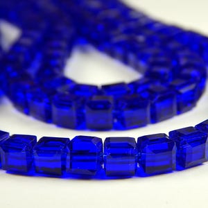 May include: A strand of bright blue square glass beads. The beads are faceted and have a shiny, reflective surface.