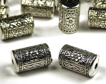 May include: Silver metal beads with a floral design. The beads are cylindrical and have a hole through the center.
