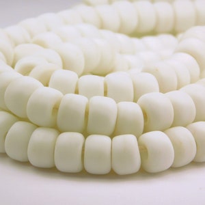 May include: A strand of white round beads, made of smooth, polished material. The beads are arranged in a circular pattern, creating a visually appealing texture.