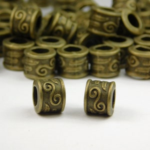 May include: Bronze-colored metal beads with a cylindrical shape and intricate swirl designs. These decorative beads are ideal for jewelry making and crafting projects. The beads have a vintage or antique appearance.