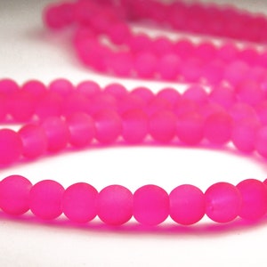 May include: A strand of bright pink frosted glass beads. The beads are round and have a matte finish.