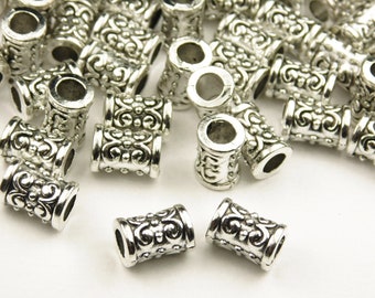May include: A pile of silver metal beads with an ornate design. The beads are cylindrical and have a hole in the center.