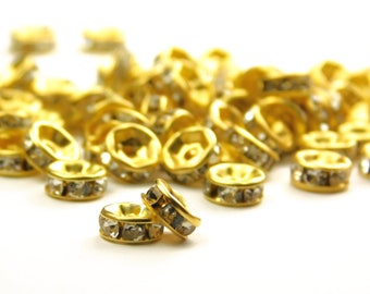 May include: A pile of gold-toned metal bead caps with clear rhinestones. The bead caps are round and have a flat top and bottom.
