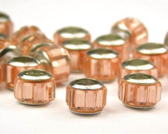 May include: A group of peach-colored glass beads with silver accents. The beads are faceted and have a shiny finish.
