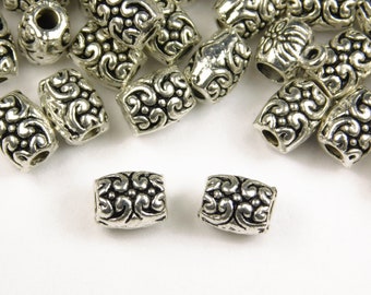 May include: Silver metal beads with a decorative floral pattern. The beads are cylindrical and have a hole in the center for stringing.