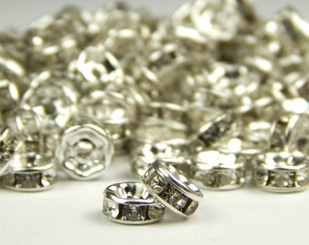 May include: A pile of silver-toned metal bead caps with clear rhinestones. The bead caps are round and have a flat top and bottom. The rhinestones are set in a circle around the edge of the bead cap.