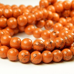 May include: A strand of orange glass beads with black swirl designs. The beads are round and have a glossy finish.