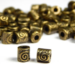 May include: A pile of antique gold metal beads with a swirling design. Two beads are isolated in the foreground.