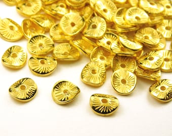 May include: A pile of gold-colored metal beads with a decorative design. The beads are shaped like a half-circle with a hole in the center.