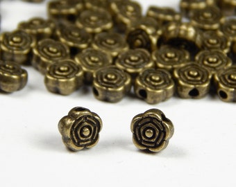 May include: A pile of antique gold metal flower-shaped beads with a hole in the center of each bead. Two beads are isolated in front of the pile.