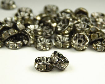 May include: A close-up of two black metal ring spacers with clear rhinestones. The spacers are on a white surface.