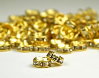 May include: Two gold-toned rings with clear crystal accents. The rings are stacked on top of each other. The rings are surrounded by a pile of similar rings.
