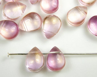 Op de afbeelding: Een groep van regenboogkleurige roze glazen druppelvormige kralen met een gouden schittering. Twee kralen zijn geregen op een zilveren draad.