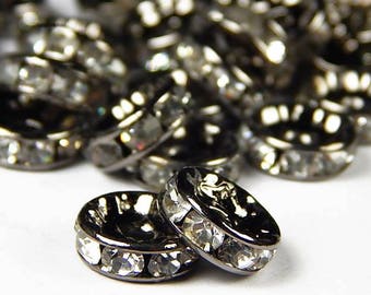 May include: A pile of black metal bead spacers with clear rhinestones. The spacers are round and have a flat back.