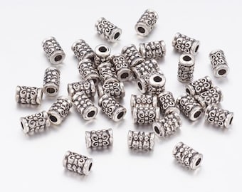 May include: A pile of silver-toned metal beads with an ornate design. The beads are cylindrical and have a decorative pattern.