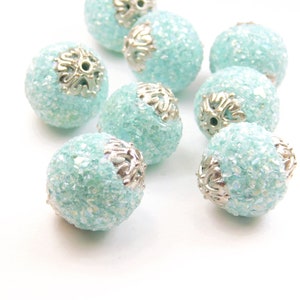 May include: A collection of light blue round beads with silver accents. The beads have a sparkly, textured surface.