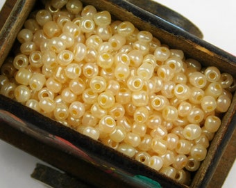 May include: A close-up of a wooden box filled with small, round, cream-colored beads with a pearlescent finish.