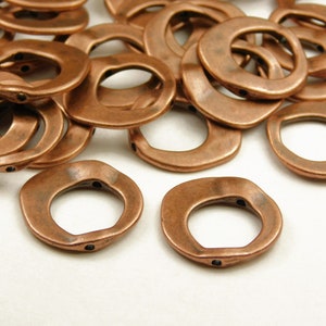May include: A pile of copper-colored metal rings with a slightly irregular, hammered finish. The rings are about 1 inch in diameter and have a hole in the center.