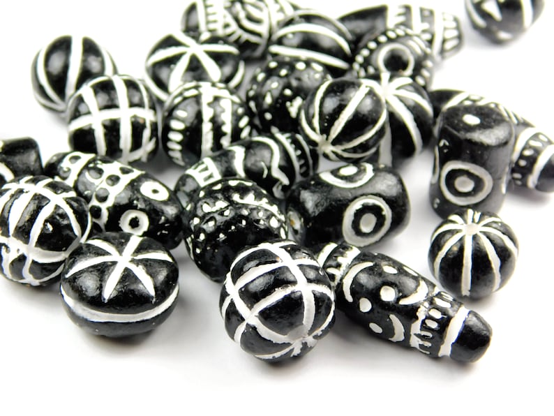 May include: A collection of black and white ceramic beads with various geometric and abstract designs. The beads are smooth and glossy, with white patterns on a black background.