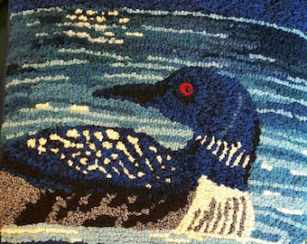 May include: A blue and white hooked rug depicting a loon swimming in a blue lake. The loon has a red eye and a white breast.