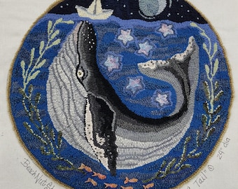 May include: A blue and gray whale with a tail curled up, swimming in a dark blue ocean with white stars. The whale is surrounded by green seaweed and orange fish. The text "A whale of a Tail" and "Beach Nut Studio" are visible in the image.