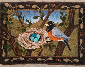 May include: A rug hooking depicting a robin perched on a branch with a nest of blue eggs. The nest is made of twigs and is surrounded by green leaves. The background is a brown and green forest scene.