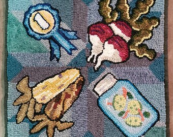 May include: A colorful rug with a blue ribbon with a number one on it, a corn cob, a jar of pickles, and a bunch of radishes.