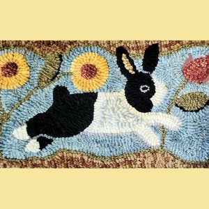 May include: Hand-hooked rug featuring a black and white rabbit leaping across a light blue background. Two yellow sunflowers and a red flower are on either side of the rabbit. The rug has a brown border.