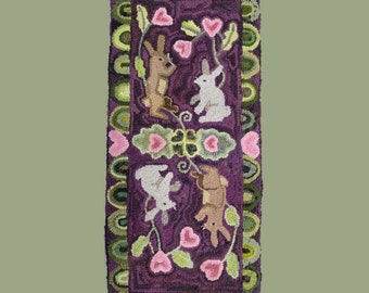 May include: A purple rug with a repeating pattern of green leaves, pink hearts, and white rabbits. The rug has a green and white border.