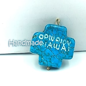 Könnte beinhalten: Ein türkisblauer Kreuzanhänger mit den Worten "Cowboy Away" in weiß. Der Anhänger hat oben eine goldene Öse zum Anbringen an einer Halskette oder einem Armband.