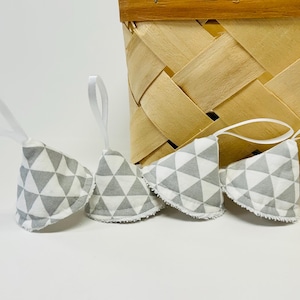 May include: Four small, cone-shaped fabric ornaments featuring a gray and white geometric triangle pattern. Each ornament has a white ribbon loop attached to the top for hanging and a white scalloped edge along the bottom base.
