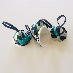 May include: Four black and white fabric cone-shaped ornaments with a white fleece lining and a black ribbon loop. The fabric has a colorful abstract pattern with green, yellow, and white shapes.