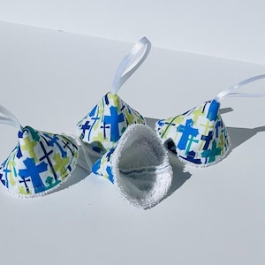 May include: Four white fabric cones with blue and green cross patterns. Each cone has a white ribbon loop attached.