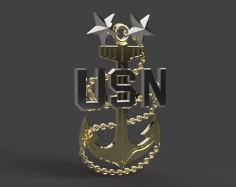 Może przedstawiać: Złoty kotwica z czarnym napisem "USN" i dwiema srebrnymi gwiazdami na górze. Kotwica jest otoczona złotym łańcuchem.