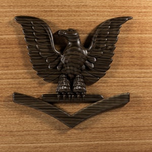 Könnte beinhalten: Ein hölzerner Adler mit ausgebreiteten Flügeln, der auf einem hölzernen Chevron sitzt. Der Adler und der Chevron sind dunkelbraun.