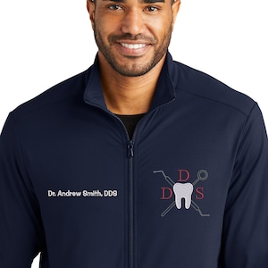 May include: A navy blue zip-up jacket with a white tooth and dental tools logo embroidered on the chest. The text "Dr. Andrew Smith, DDS" is embroidered below the logo.