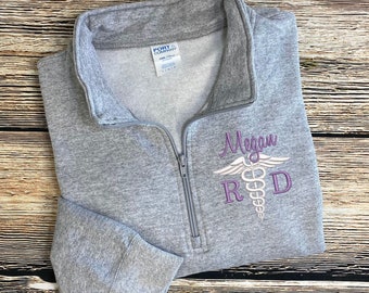 May include: Gray zippered sweatshirt with a purple embroidered medical symbol and the name Megan and the letters R.D.