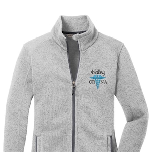 May include: A gray fleece zip-up jacket with a blue and white embroidered medical symbol and the text "Haley CRNA".