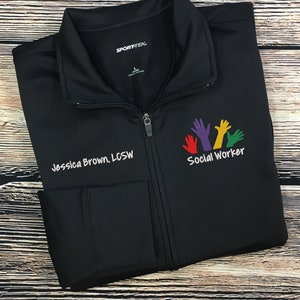 May include: Black zippered jacket with a white embroidered logo that says "Social Worker" and a white embroidered name "Jessica Brown, LCSW".