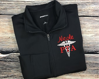 May include: Black zippered jacket with a red embroidered name "Nicole" and a silver medical symbol with the letters "PTA" underneath.